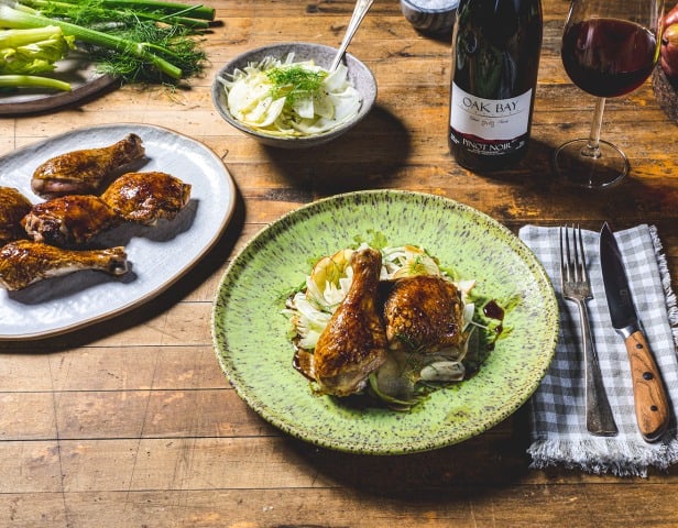 A plate of roast chicken and Oak Bay Pinot Noir at a dinner table - one of our favorite wine pairings.