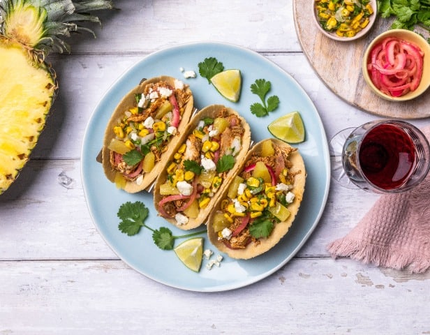 A plate of chicken Tacos with corn, cheese, onion, cilantro, and lime