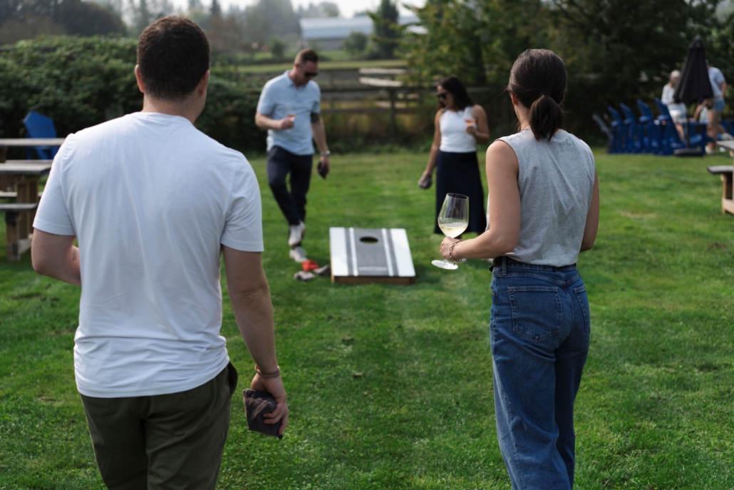 A group playing cornhole while drinking glasses of wine at Backyard Vineyards in Langley, BC.