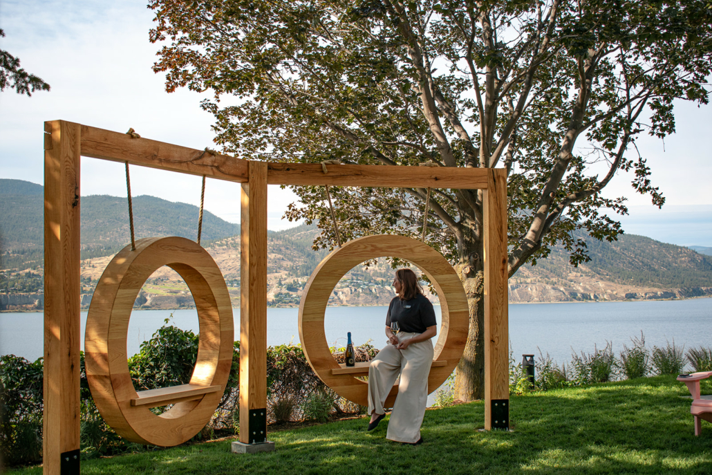 A woman sits on the swing at Evolve Sparkling House with a glass of sparkling wine looking out at the view of Okanagan Lake.