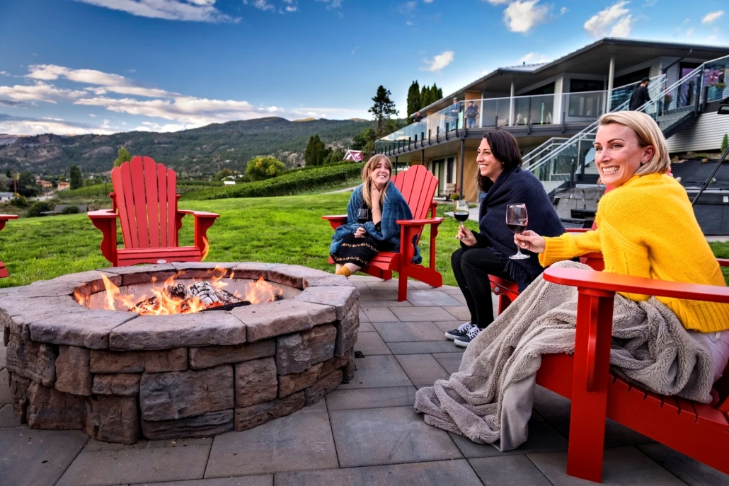 A group of women sitting around the fire with a glass of wine at Therapy Vineyards in Naramata, BC.