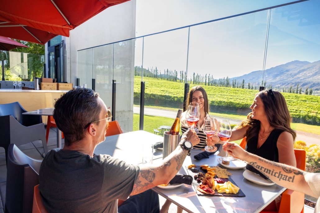 A group cheers their wine glasses on the sunny patio with vineyard views at The Terrace Restaurant at Monte Creek Winery in Kamloops, BC.