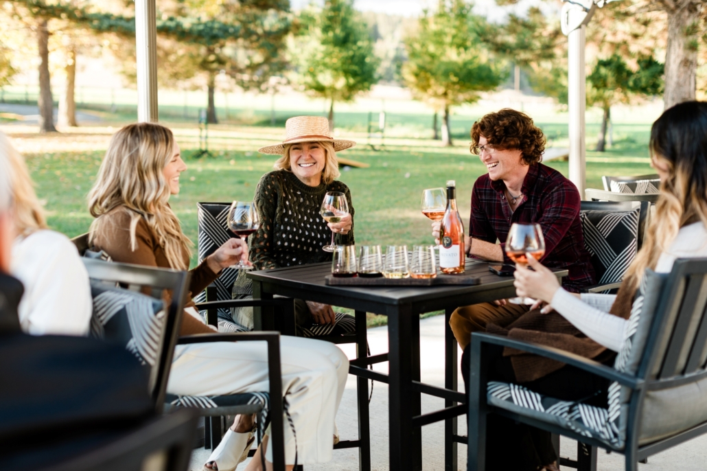 A group of visitors smiles as they enjoy their wine on the scenic Privato Vineyard & Winery patio during fall, located in Kamloops, British Columbia.