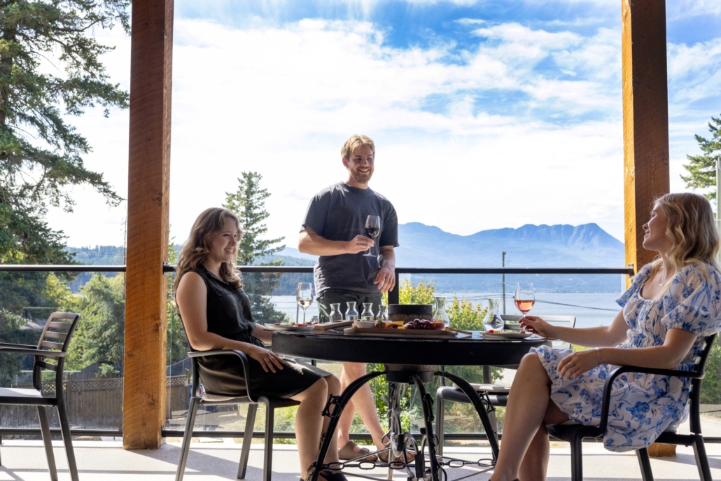 A group wine-tasting on the patio at Sunnybrae Winery in the Shuswap with the scenic Shuswap lake and mountains in the background.